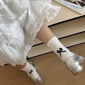 Close-up of white crew socks with black bow detail paired with silver Mary Jane shoes
