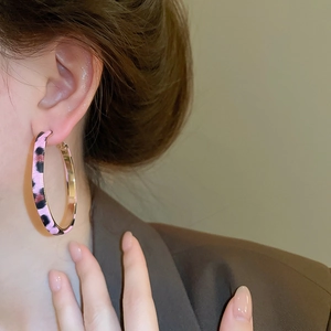 Close-up of pink leopard print hoop earrings worn by a model in soft lighting