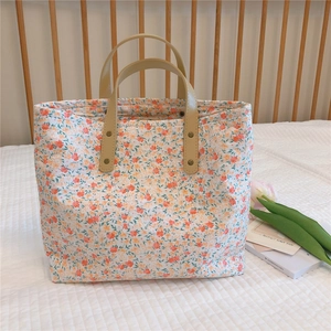Close-up of floral tote bag with orange blossoms and beige leather handles