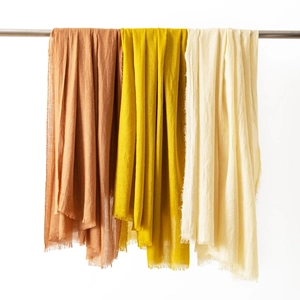 Three premium cotton linen scarves in brown yellow and beige with fringe hanging on a rod