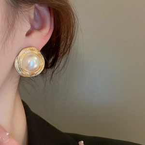 Close-up of vintage gold brushed metal stud earrings with large white pearls on a model