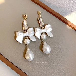Elegant gold bow earrings with pearls and rhinestones on a textured background