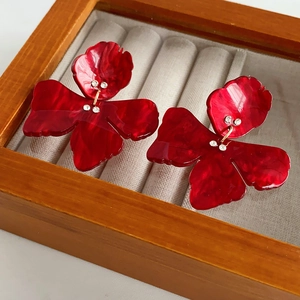 Detailed shot of red resin flower earrings with sparkling rhinestones on beige velvet padding