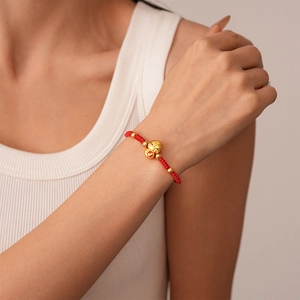 Close-up of a red woven bracelet featuring a golden Maneki-neko cat charm on a wrist