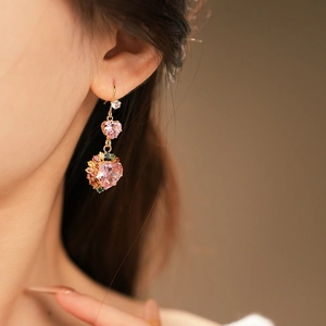 Close-up of golden earring with pink heart stones and colorful zircon accents on model