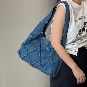 Detail showing the textured blue denim fabric and gold logo on the shoulder bag