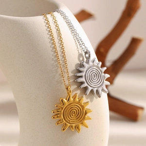 Detail of sun pendant necklaces in gold and silver finish hanging on a white ceramic vase