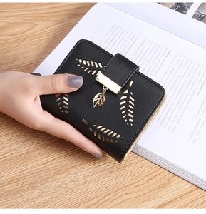 Detail of black small wallet featuring gold leaf patterns and leaf-shaped metal pendant