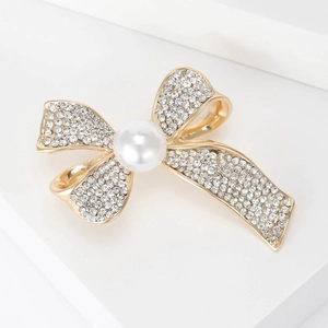 Detailed macro view of golden bow brooch with sparkling rhinestones and a white pearl accent