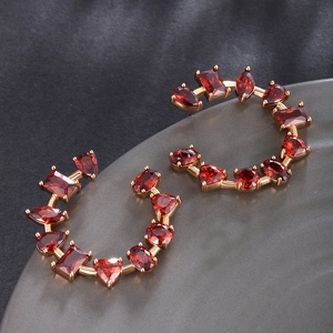 Detail of gold C-shaped hoop earrings featuring colorful mixed-cut red zircon stones