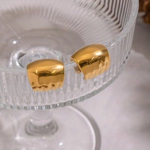 Detail of gold wide half-round cuff earrings with wavy texture on a glass tray