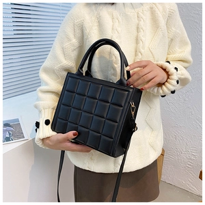 Detail of black quilted leather square handbag with top handle and gold metal buckles