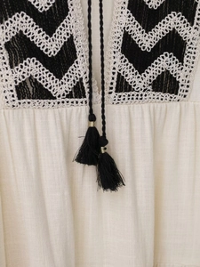 Detail of cream dress neckline featuring black wave embroidery and tassel ties