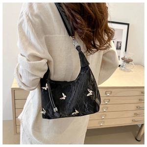 Detail of black pleated shoulder bag with silver butterfly charms on a female model