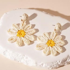 Close-up of handmade woven daisy drop earrings with white petals and yellow centers