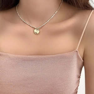 Detailed close-up of a silver bead chain with a textured gold coin pendant on the collarbone
