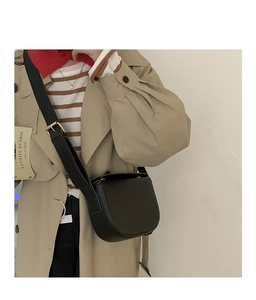 Close-up of a black PU leather saddle bag with wide shoulder strap and gold hardware