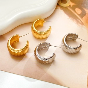 Detailed view of C-shaped ribbed metal earrings in gold and silver finish with textured surface