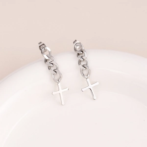 Macro shot of silver cross earrings with curb chain tassels on a white ceramic plate