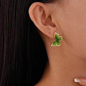 Elegant gold butterfly stud earrings with green zircon crystals on a model's ear