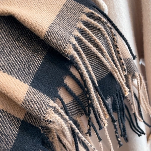 Close-up of camel and black plaid knit scarf showing soft texture and fringe details