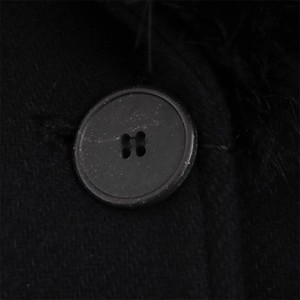 Détail d'un bouton noir en résine sur un manteau en laine avec col en fausse fourrure