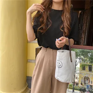 Detail of white canvas bucket bag with smiling face print and brown leather handle