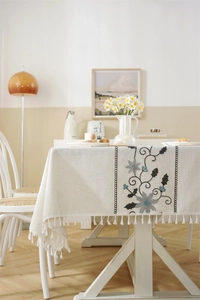 Detail showing 3D floral embroidery and white fringe on a linen-blend tablecloth