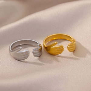 Close-up of gold and silver hugging hands open rings on a beige silk fabric surface
