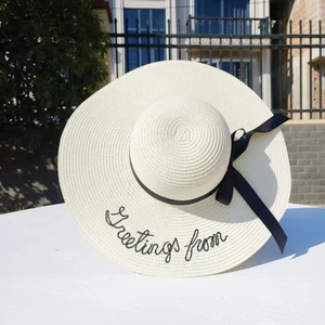 Close-up of beige straw hat with black ribbon and Greetings from embroidery detail