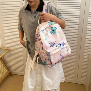 Pink butterfly and daisy print canvas backpack for students shown on a female model