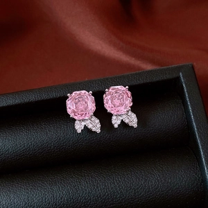 Close-up of pink crystal rose stud earrings with cubic zirconia leaves on black leather
