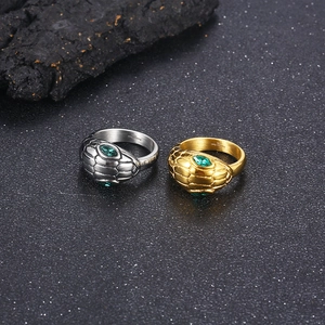 Detail of gold and silver snake rings with green stone eyes on dark stone surface