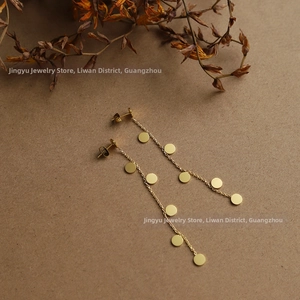 Detail of long gold chain earrings with multiple round disc charms on a rustic background