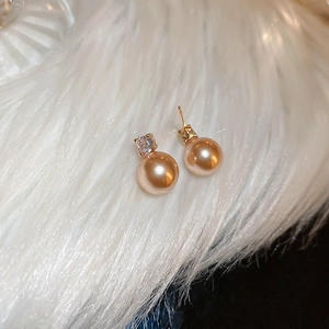 Macro shot of elegant champagne pearl earrings with zircon inlay on white faux fur