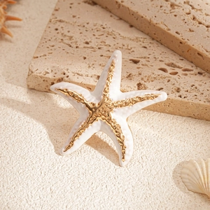 Detail of white starfish ring with gold trim on natural stone and sand background