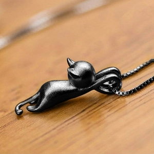 Macro shot of matte black cat pendant with stretch posture on a warm wood surface