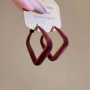 Détail de boucles d'oreilles géométriques bordeaux avec finition velours et flocage mat