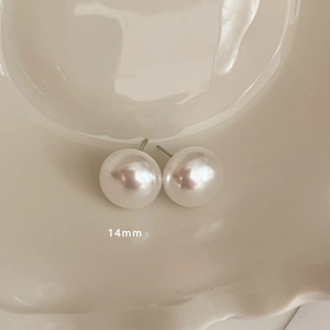 Macro detail of 14mm large pearl earrings on a textured cream ceramic dish