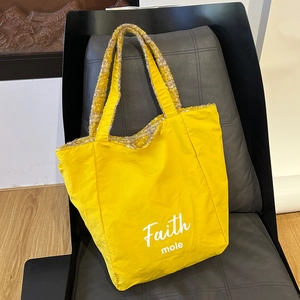 Detail of yellow nylon tote bag with Faith logo and plush fleece trim on black chair