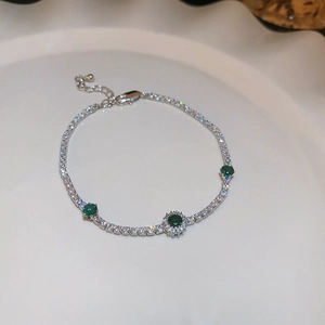 Close-up of silver bow bracelet with green zircon gemstones on a ceramic plate