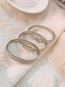 Close-up of three silver-plated vintage bangles with heart and wheat textures on knit background