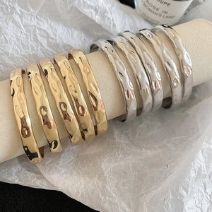 Detailed close-up of gold and silver hammered metal bangles on a minimalist white stand