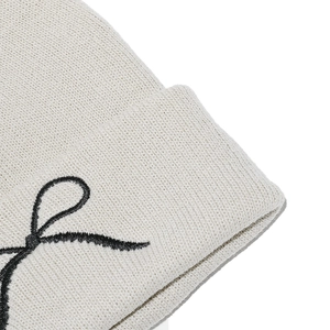 Close-up of cream knit beanie featuring detailed texture and black ribbon pattern