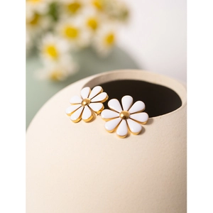 Close-up of gold stainless steel daisy earrings with white enamel petals on a ceramic dish