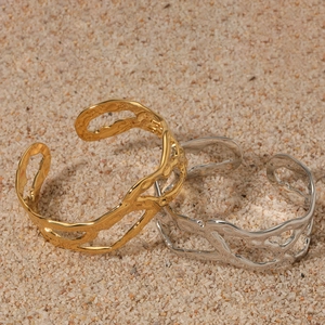 Moderni bracciali aperti traforati in oro e argento su sfondo di pietra naturale