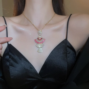 Detail of a gold necklace with fan-shaped pendant and pink purple gems on a black outfit