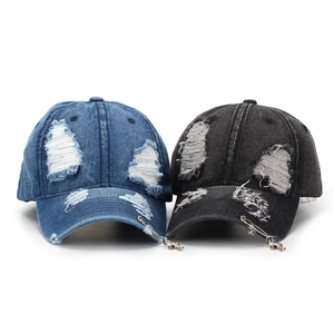 Detail of distressed denim baseball caps with cross pendants and safety pin accents