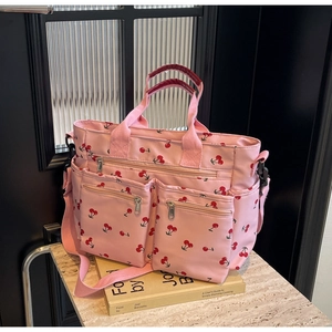 Pink nylon tote bag with cherry print and multiple zipper pockets on a marble surface