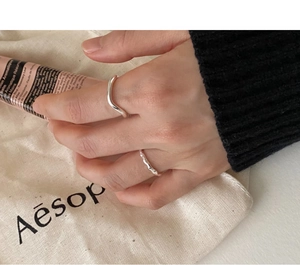 Minimalist wavy silver rings on finger set against elegant canvas and cream tube